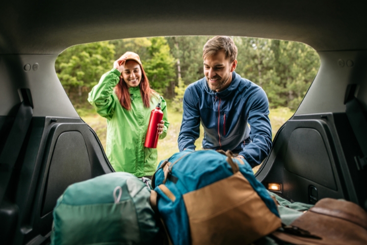 happy couple taking out luggage from car trunk