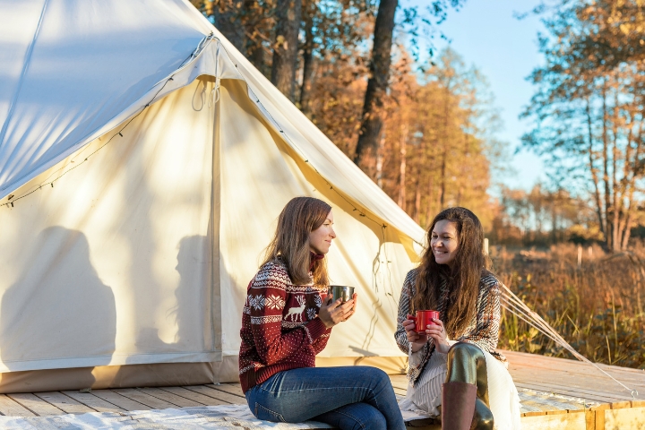 two girls holding mugs outside glamping tent