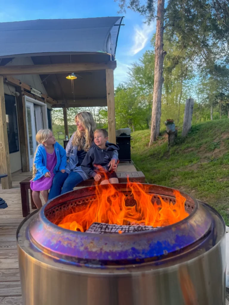 a mom and her children sitting by the Solo Stove fire pit outside of a glamping tent